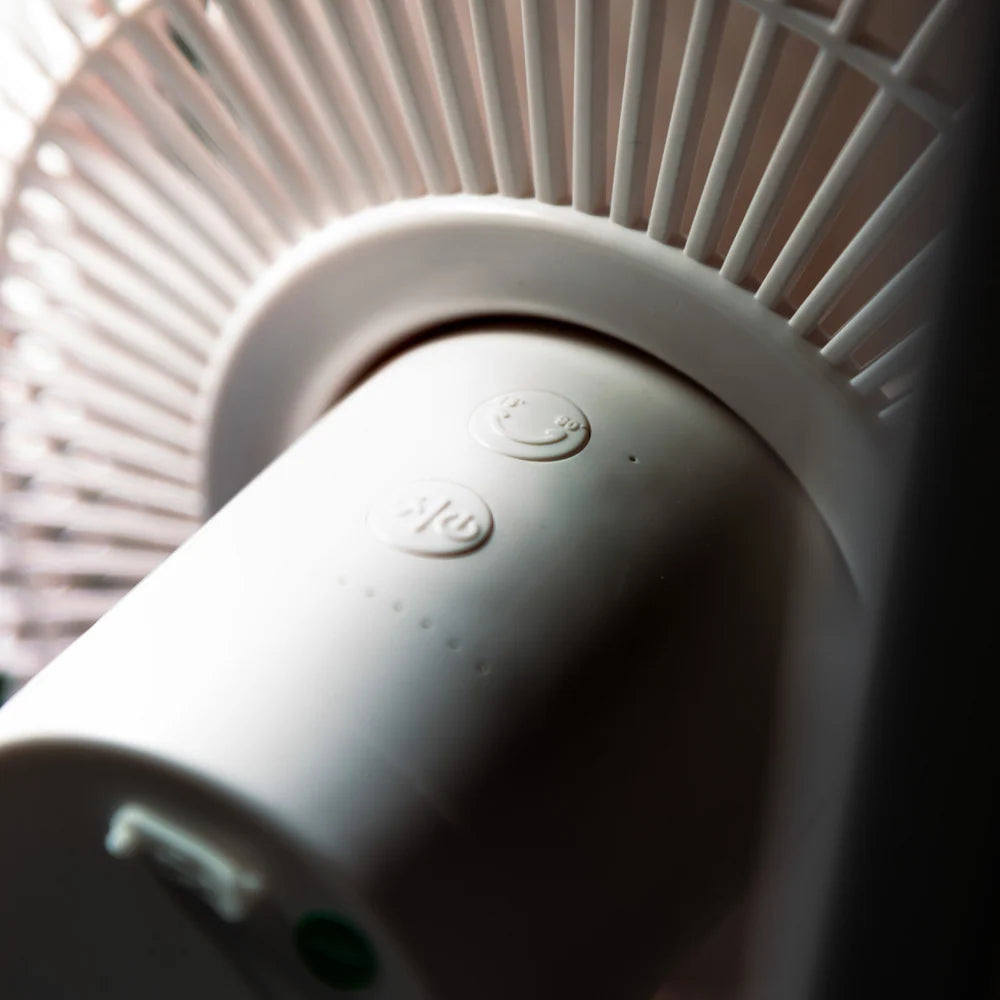 A close-up shot of a white cylindrical fan motor housing, with ribbed detailing and small circular buttons on the top surface.