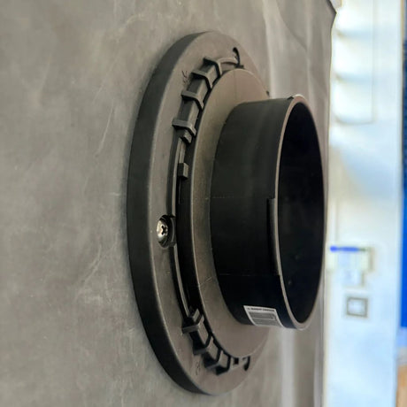 A black plastic duct fitting photographed on a gray textured surface with a blurred indoor background.