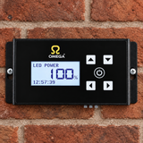 An Omega LED power controller with a black faceplate and blue backlit display, mounted on a red brick wall.