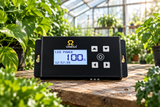 Omega Synco LED driver controller for plant grow lights, shown in a greenhouse setting on a wooden table surrounded by green plants.